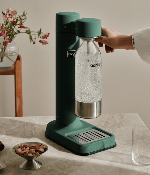 Aarke Carbonator 3 in Heritage Green carbonating water in a stainless steel bottle on a marble countertop.