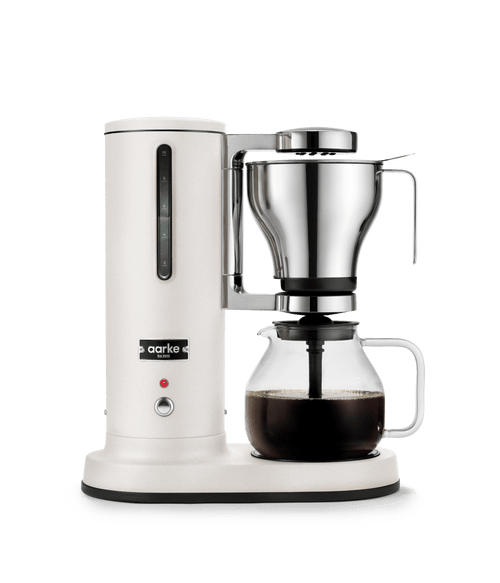 Aarke matte white automatic pour-over coffee maker with stainless steel filter brewing coffee into glass carafe.