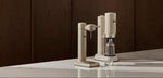 Aarke sparkling water makers in beige on a kitchen countertop with a water bottle and glass, showcasing minimalist Scandinavian design. Save 20% off on sparkling water makers and water filter pitchers.