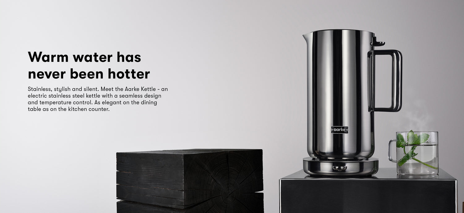 Aarke Stainless Steel Kettle sits beside a hot cup of mint tea. Text reads: Warm water has never been hotter. Stainless, stylish and silent. Meet the Aarke Kettle - an electric stainless steel kettle with a seamless design and temperature control. As elegant on the dining table as on the kitchen counter.