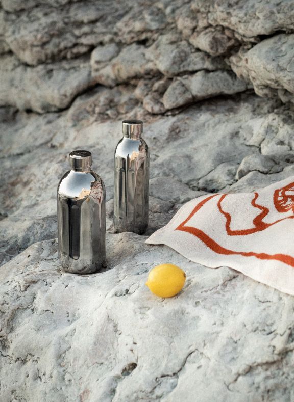 Two metallic bottles and a lemon on a rocky surface with a towel.