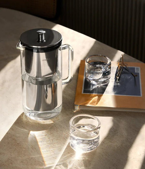 Aarke Purifier on marble table with two glasses of water and a magazine with reading glasses.