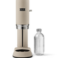 Aarke Carbonator Pro in Sand. Front view with chamber open. Glass bottle is sitting beside the Carbonator.