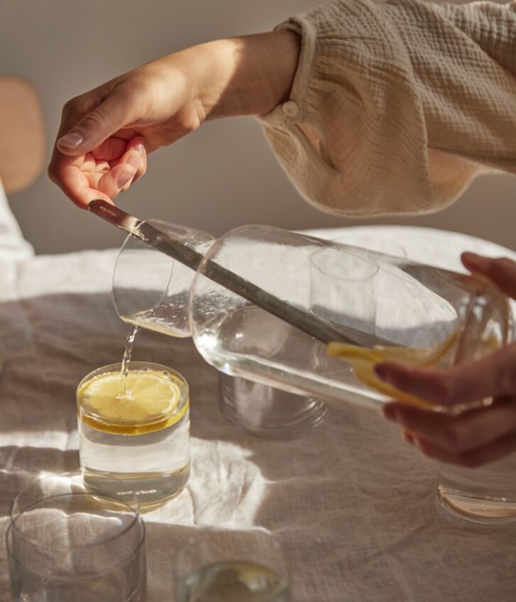 A person pours water into a glass with a lemon from the Nesting Carafe/