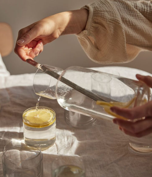 Person pouring lemon water from the Aarke glass carafe into a small glass using the mixing spoon.
